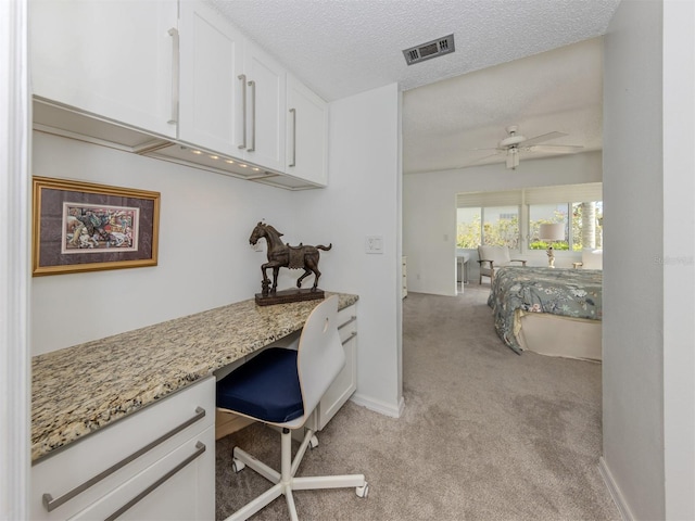 office space with visible vents, built in study area, ceiling fan, a textured ceiling, and light carpet