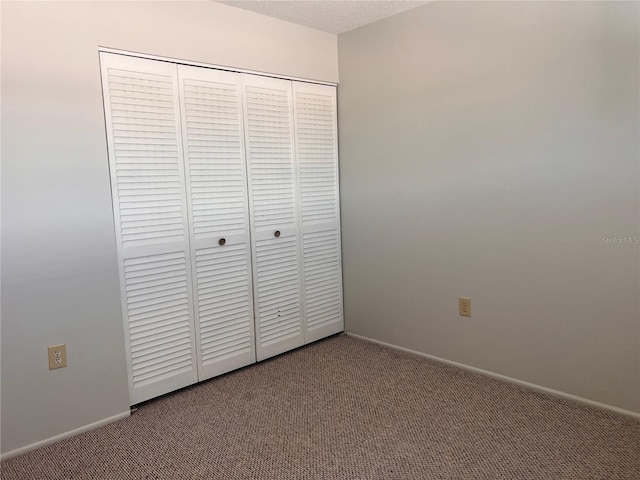 unfurnished bedroom featuring a textured ceiling, carpet, a closet, and baseboards