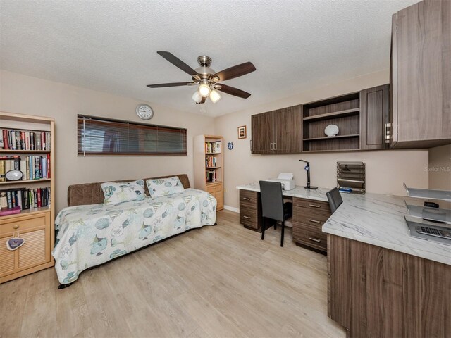 bedroom featuring ceiling fan, a textured ceiling, light wood-style flooring, and built in study area