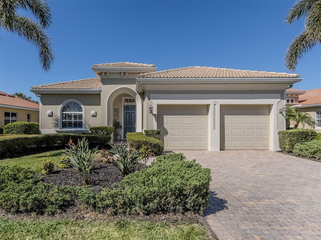 mediterranean / spanish home with a tiled roof, decorative driveway, an attached garage, and stucco siding