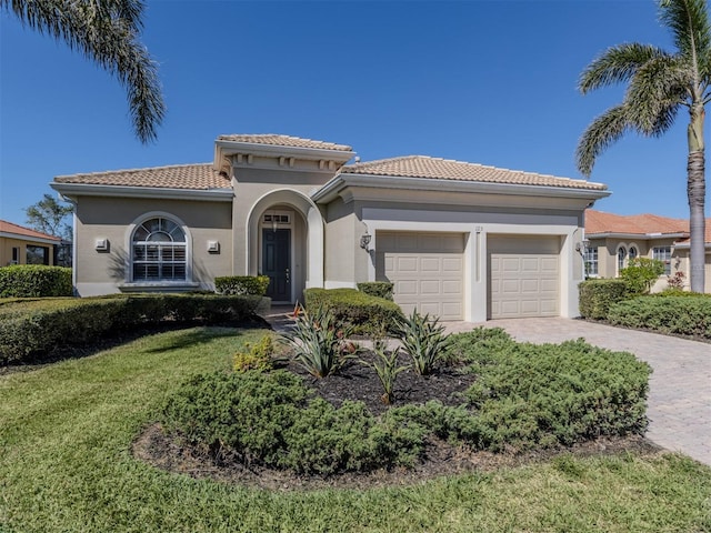 mediterranean / spanish home with a front lawn, a tiled roof, stucco siding, decorative driveway, and a garage