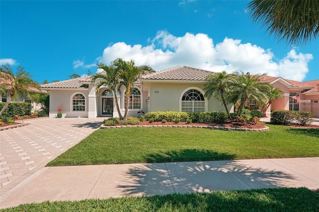 mediterranean / spanish home with stucco siding, a tile roof, and a front lawn