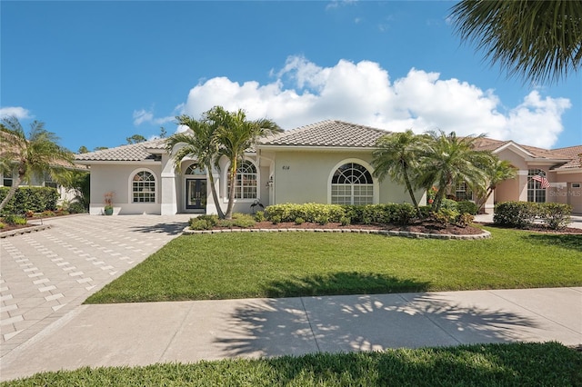 mediterranean / spanish home featuring stucco siding, a tile roof, and a front lawn