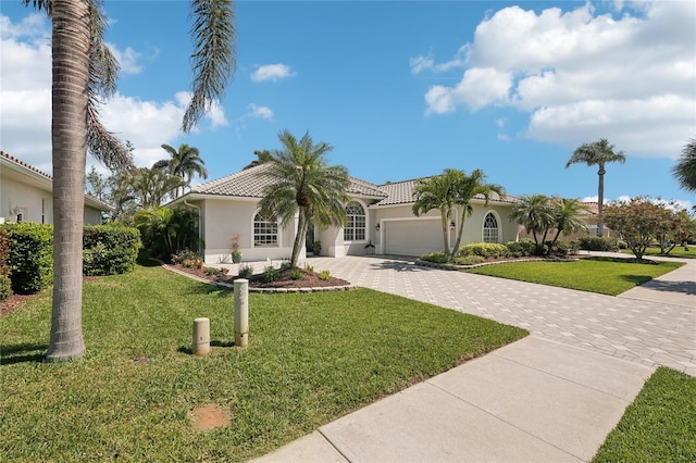 mediterranean / spanish house with a front lawn, a tiled roof, stucco siding, decorative driveway, and an attached garage