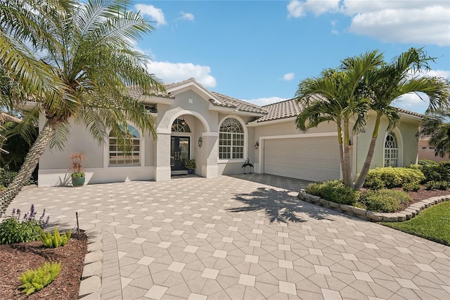 mediterranean / spanish-style home featuring an attached garage, stucco siding, french doors, a tiled roof, and decorative driveway