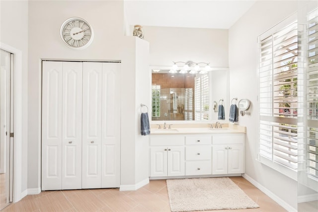 bathroom with double vanity, tiled shower, baseboards, and a sink