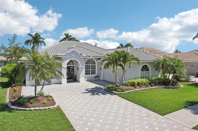 mediterranean / spanish-style house featuring stucco siding, a front lawn, decorative driveway, an attached garage, and a tiled roof