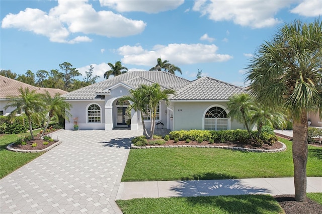 mediterranean / spanish house with a front lawn, a tile roof, stucco siding, french doors, and driveway