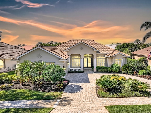 mediterranean / spanish-style house featuring french doors, decorative driveway, stucco siding, and a tile roof