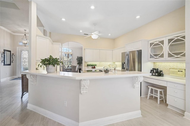 kitchen featuring stainless steel fridge with ice dispenser, a breakfast bar, ceiling fan with notable chandelier, arched walkways, and white cabinetry