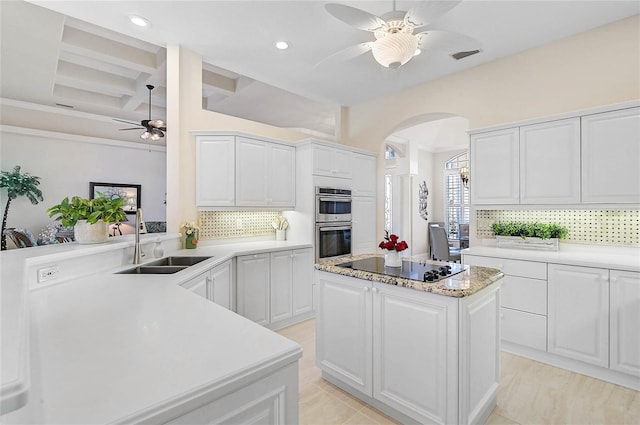 kitchen with visible vents, black electric stovetop, ceiling fan, arched walkways, and a sink