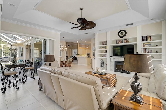 living room with built in features, a tray ceiling, and ceiling fan with notable chandelier