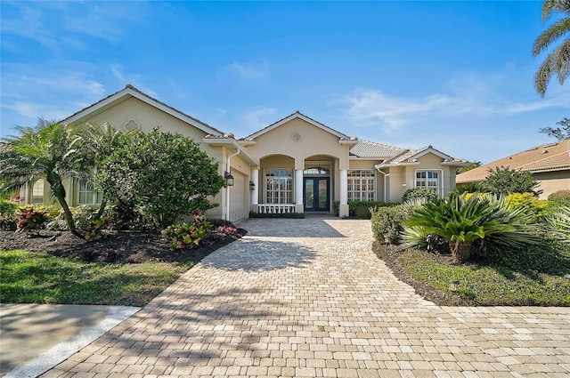 mediterranean / spanish home featuring decorative driveway, french doors, a garage, and stucco siding