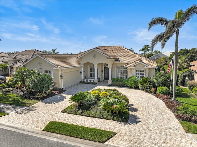 mediterranean / spanish-style home featuring a tile roof, decorative driveway, a garage, and stucco siding