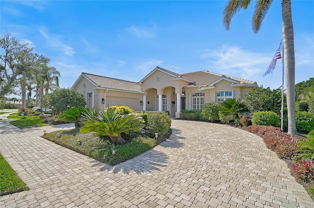 mediterranean / spanish home featuring a tile roof, decorative driveway, a garage, and stucco siding