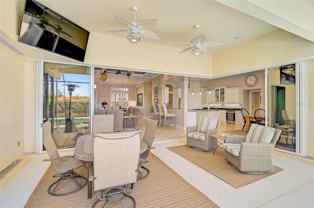 dining room featuring ceiling fan, beverage cooler, decorative columns, a high ceiling, and arched walkways