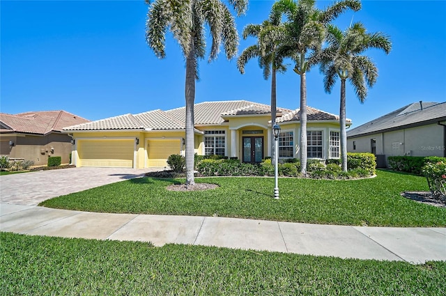 mediterranean / spanish house featuring stucco siding, a front lawn, an attached garage, and a tile roof