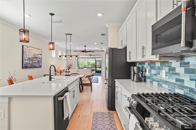 kitchen with stainless steel appliances, light countertops, visible vents, ornamental molding, and a sink