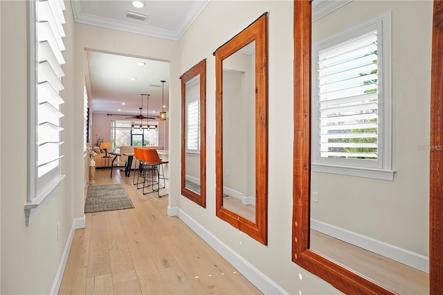 hallway featuring crown molding, visible vents, light wood finished floors, and baseboards
