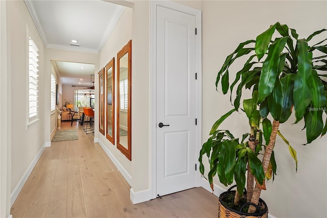 hall featuring baseboards, crown molding, and light wood finished floors