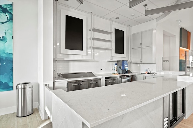 kitchen featuring tasteful backsplash, a sink, light wood-style floors, light stone countertops, and a paneled ceiling