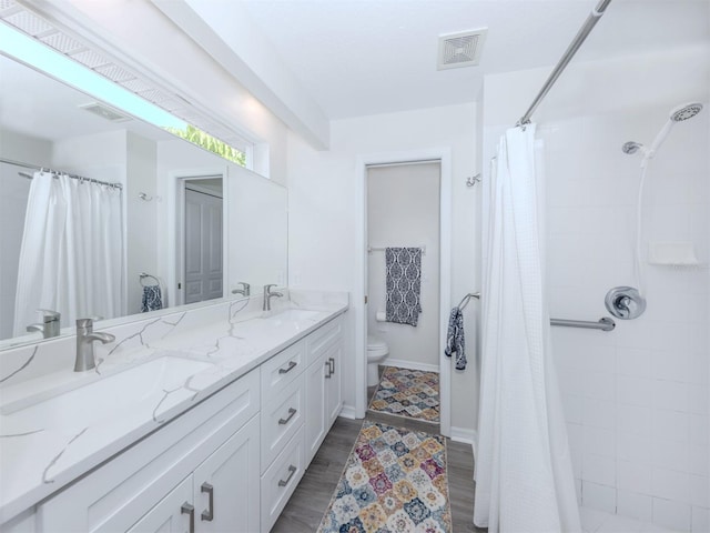 full bathroom with toilet, tiled shower, visible vents, and a sink