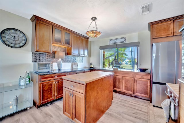 kitchen with light wood-style flooring, tasteful backsplash, freestanding refrigerator, and wooden counters