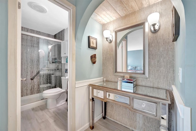 full bathroom with a wainscoted wall, wood finished floors, toilet, and a stall shower