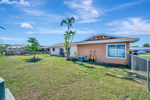 rear view of property featuring stucco siding, a lawn, central AC unit, and a fenced backyard