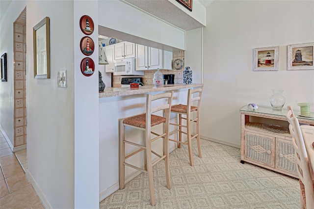 kitchen featuring a breakfast bar area, white microwave, baseboards, light countertops, and tasteful backsplash