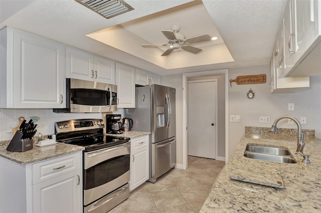 kitchen with a sink, white cabinetry, stainless steel appliances, a raised ceiling, and ceiling fan