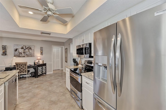 kitchen with visible vents, a ceiling fan, a tray ceiling, white cabinetry, and appliances with stainless steel finishes