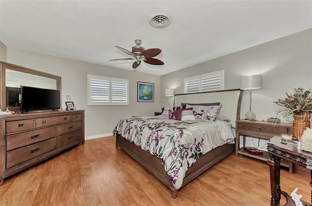 bedroom with a ceiling fan, light wood-style floors, visible vents, and baseboards