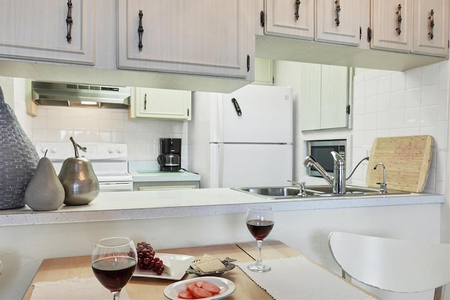 kitchen with backsplash, under cabinet range hood, light countertops, white appliances, and a sink