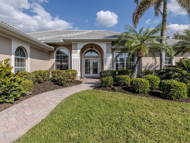 property entrance with a tiled roof, a yard, french doors, and stucco siding