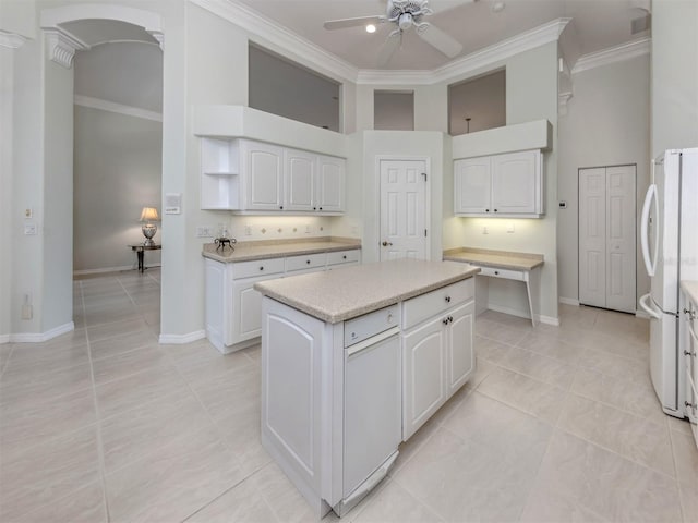 kitchen with a high ceiling, freestanding refrigerator, ornamental molding, ceiling fan, and white cabinetry