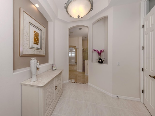 corridor featuring arched walkways, baseboards, and light tile patterned flooring