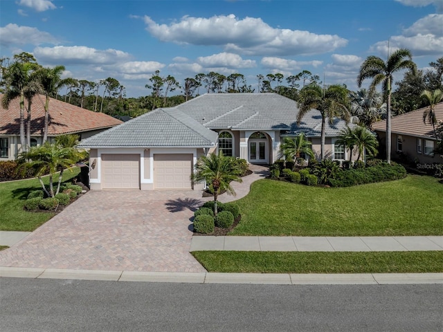 view of front of house with stucco siding, decorative driveway, a front yard, an attached garage, and a tiled roof