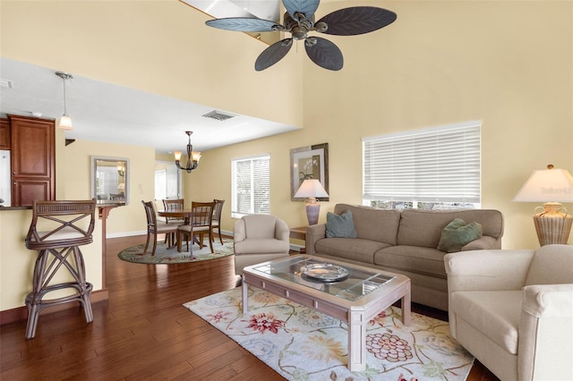 living area with visible vents, ceiling fan with notable chandelier, wood finished floors, baseboards, and a towering ceiling