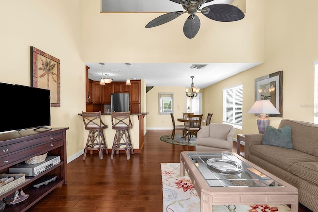 living area featuring visible vents, dark wood-type flooring, ceiling fan with notable chandelier, baseboards, and a towering ceiling