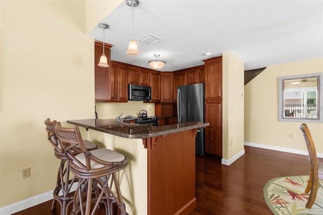 kitchen with visible vents, dark wood finished floors, freestanding refrigerator, a peninsula, and a breakfast bar area