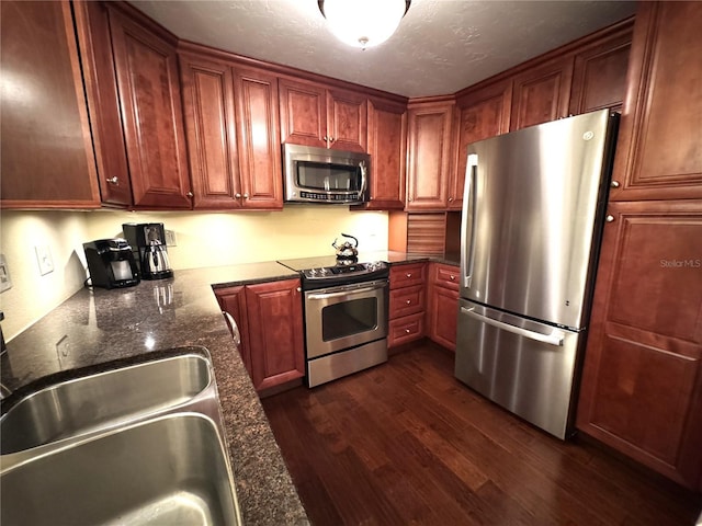 kitchen with dark stone counters, dark wood-style flooring, stainless steel appliances, a textured ceiling, and a sink