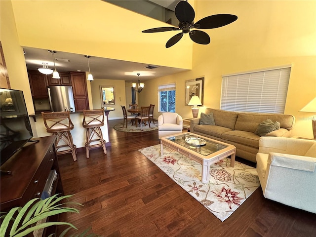 living room with visible vents, dark wood-type flooring, baseboards, a towering ceiling, and a ceiling fan