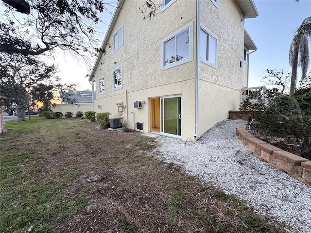 back of property with a lawn, central AC, and stucco siding