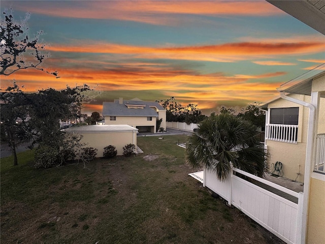 yard at dusk featuring a balcony and fence