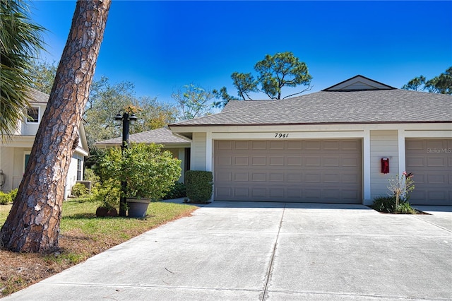 ranch-style home featuring an attached garage, roof with shingles, and driveway