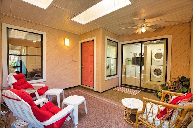 sunroom with ceiling fan, wood ceiling, a skylight, and stacked washing maching and dryer