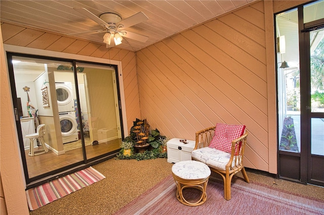 sitting room featuring wooden walls, ceiling fan, and stacked washer / dryer