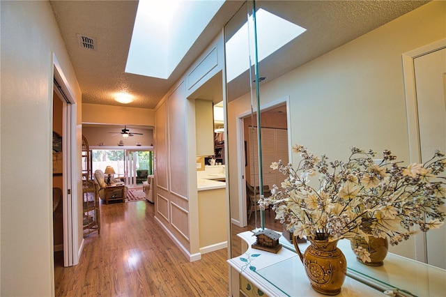 hall featuring visible vents, baseboards, a skylight, wood finished floors, and a textured ceiling