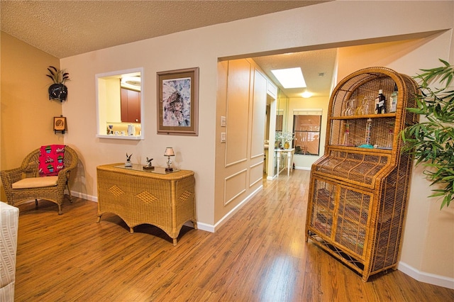 hall featuring light wood-style flooring, a textured ceiling, and baseboards